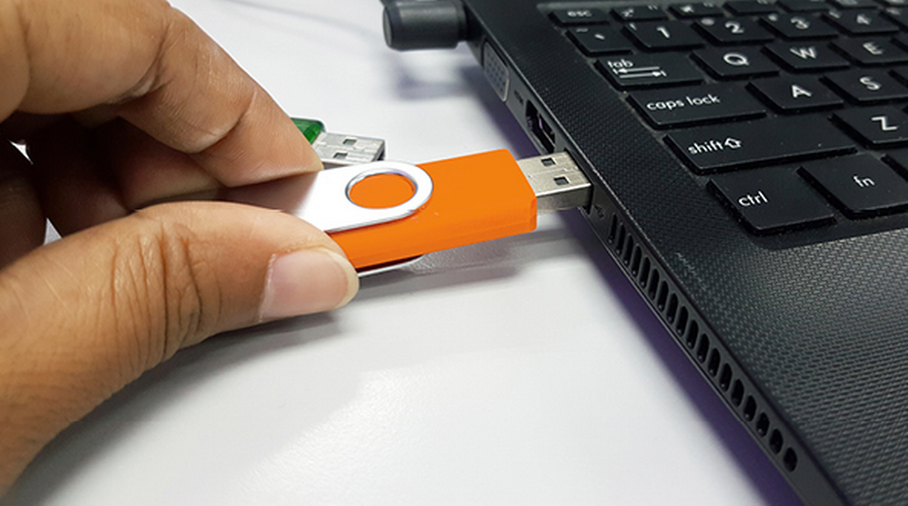 Hand inserts a USB stick into the side of a laptop