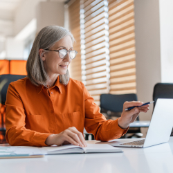 Geschäftsfrau arbeitet am Laptop und hält dabei ein Smartphone am Schreibtisch in der Hand