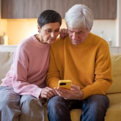Zwei ältere Menschen beugen sich auf einem Sofa sitzend über ein Smartphone